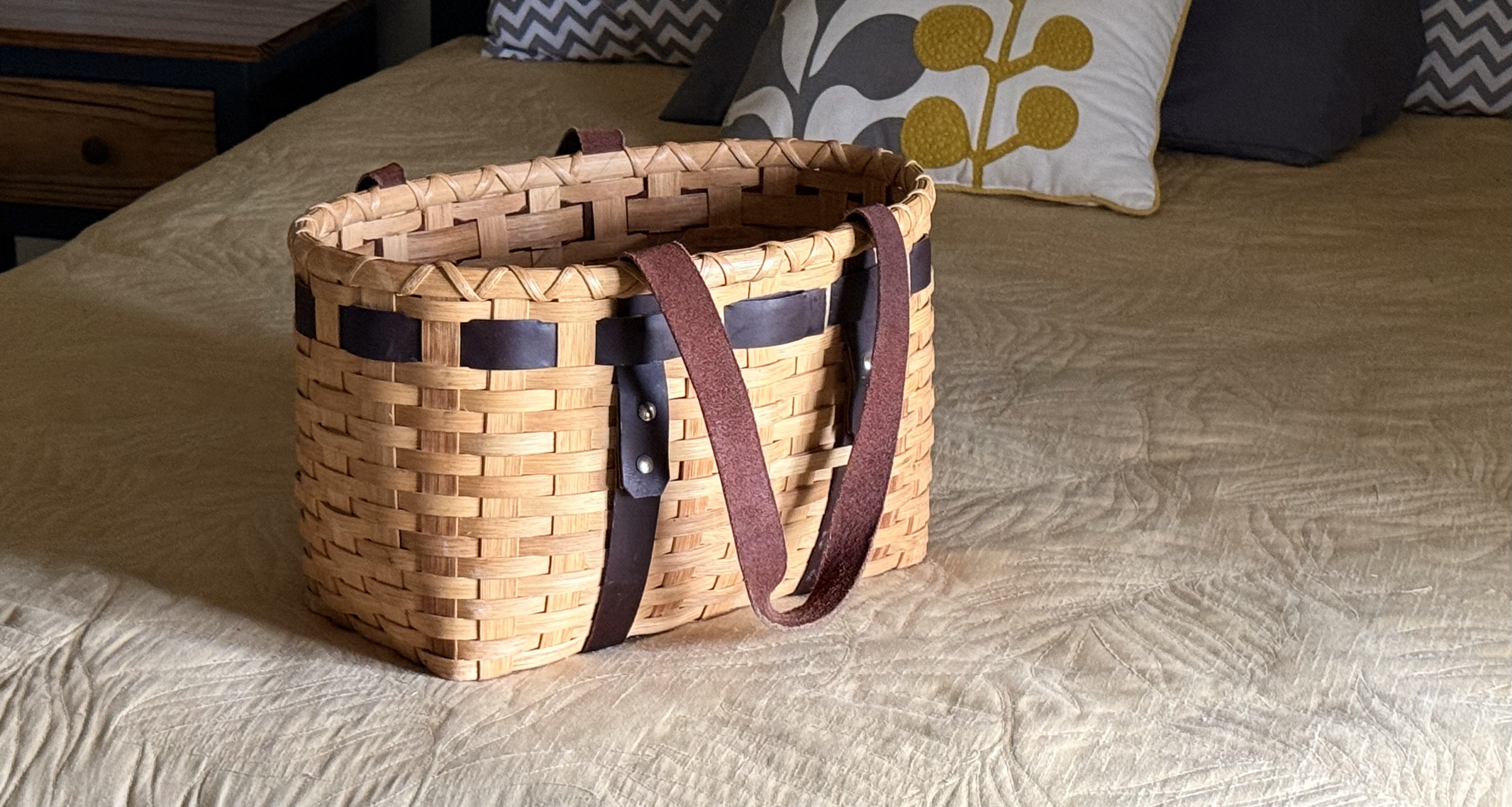 A handwoven reed tote basket with leather handles packed on a bed